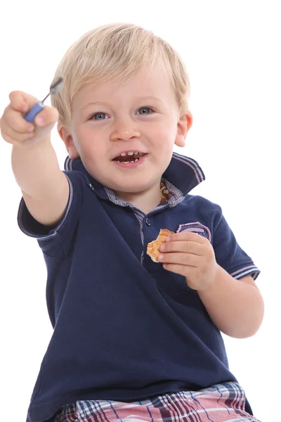 Niño comiendo una galleta y jugando con la varita de rímel de mamá —  Fotos de Stock