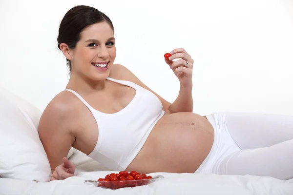 A pregnant woman eating strawberries on her bed. Royalty Free Stock Images