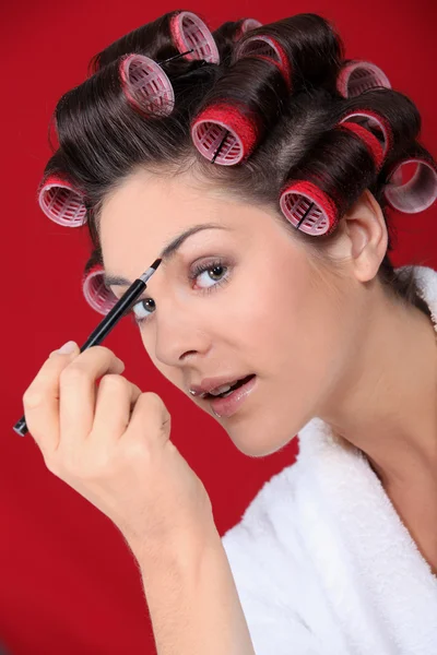 Woman with curlers putting on makeup — Stock Photo, Image