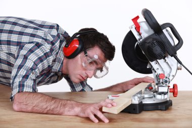 Man positioning a plank of wood in a mitre saw clipart