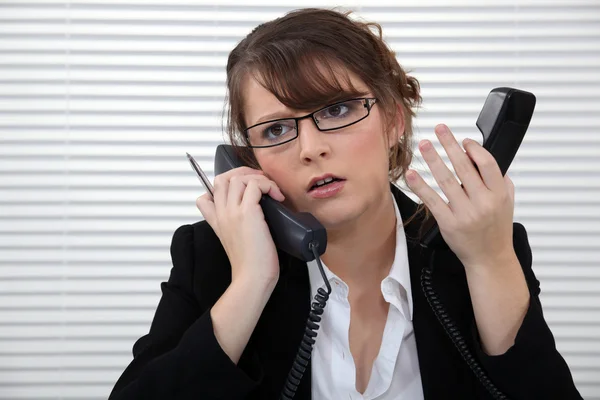 Gestresste Büroangestellte mit zwei Telefonen — Stockfoto