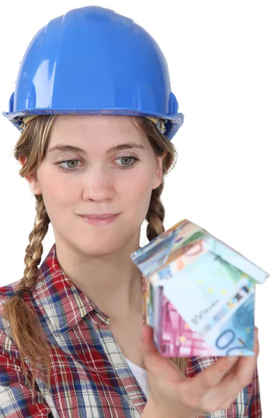 Female builder holding house made from bank notes — Stock Photo, Image