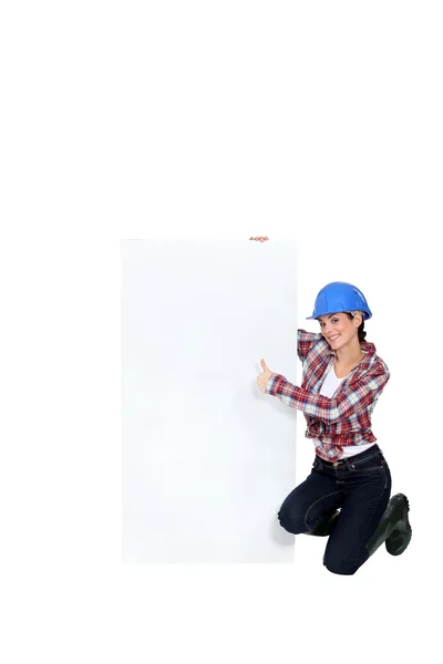 Morena constructor dando pulgares hacia arriba por el cartel en blanco — Foto de Stock