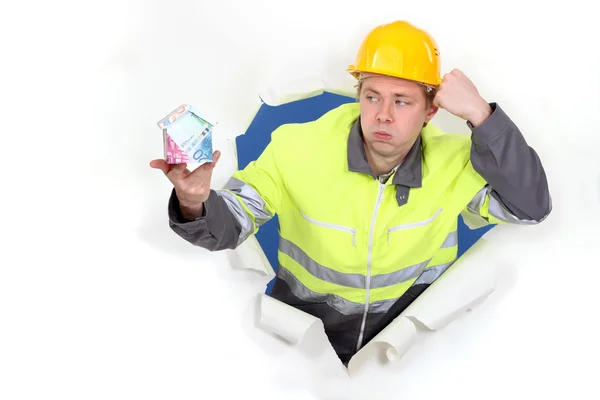 A handyman presenting a miniature house made of euro bills. — Stock Photo, Image