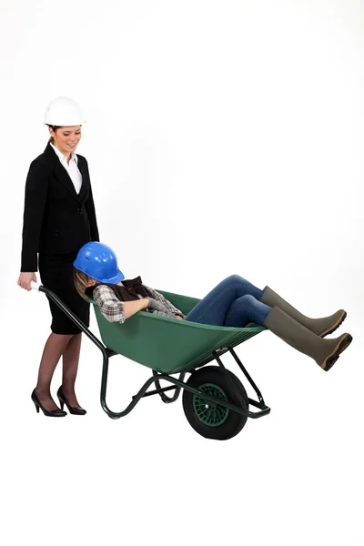 Mulher empurrando colega sonolento em um carrinho de mão — Fotografia de Stock