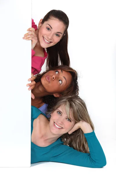Três jovens mulheres atrás do painel branco — Fotografia de Stock