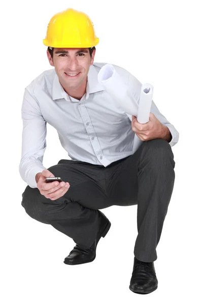 Architect kneeling with mobile and plans — Stock Photo, Image