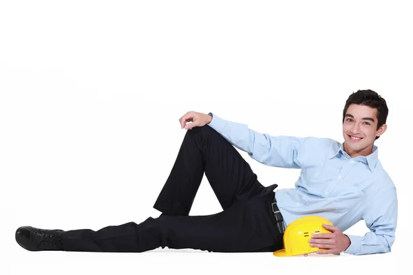 Portrait of young foreman lying on floor with hard hat — Stock Photo, Image