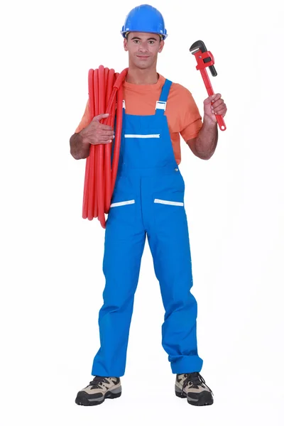 Tradesman holding corrugated tubing and a pipe wrench — Stock Photo, Image