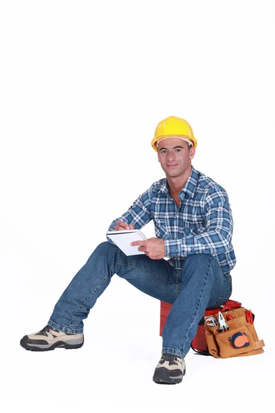 Artesano con cuaderno sentado en la caja de herramientas — Foto de Stock