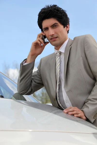 Annoyed businessman talking on his mobile phone by his car — Stock Photo, Image