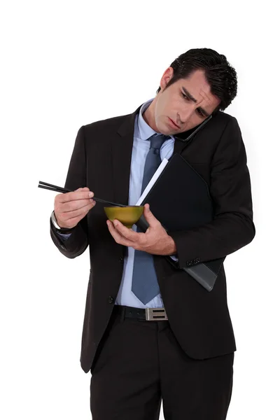 Empresário tentando comer macarrão enquanto fala ao telefone — Fotografia de Stock