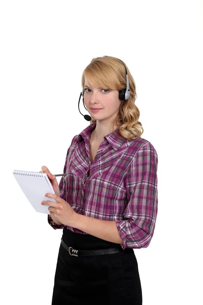 Woman in a headset writing in a notepad — Stock Photo, Image