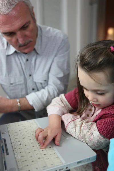 Ragazzina con computer portatile e nonno guardando su di lei — Foto Stock