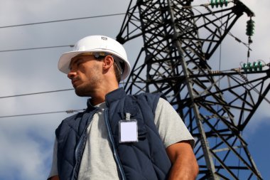 Worker standing in front of an electricity pylon clipart