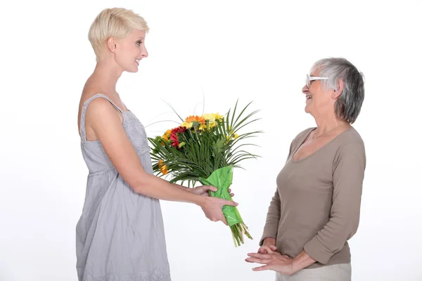 Junge Frau schenkt ihrer Großmutter einen Blumenstrauß — Stockfoto