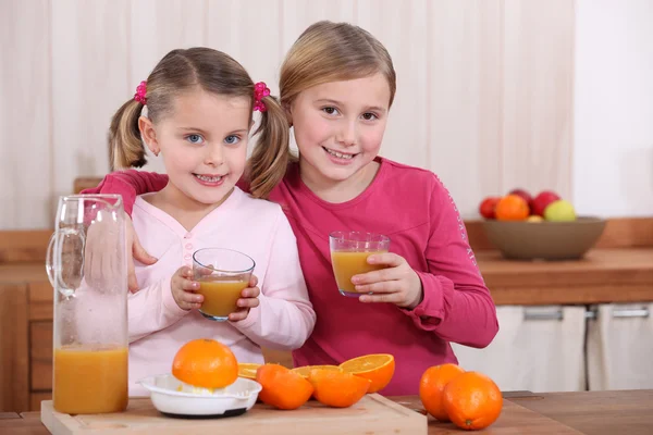 Two sisters drinking orange juice in kitchen — Stock Photo, Image