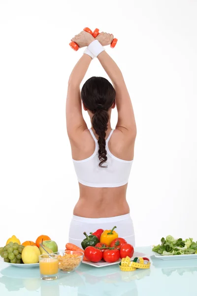 Healthy food on table and sporty woman back turned — Stock Photo, Image
