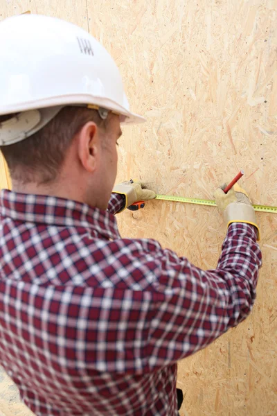 Homem usando fita métrica para marcar painel de madeira — Fotografia de Stock