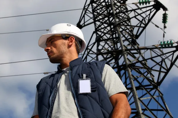 Trabalhador em pé na frente de um pilão de eletricidade — Fotografia de Stock