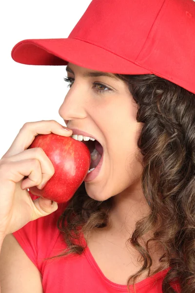 Брюнетка в красной кепке, кусающаяся в яблоко — стоковое фото