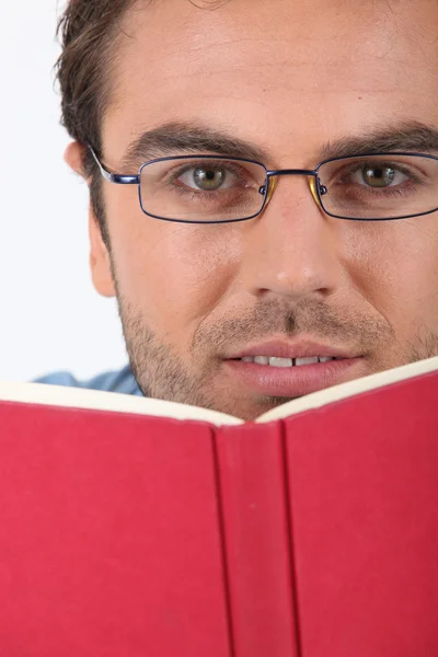 Homme en lunettes lisant un livre de dos rouge — Photo