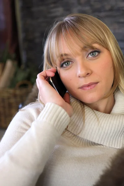 Blond woman making phone call whilst sat on cosy sofa — Stock Photo, Image