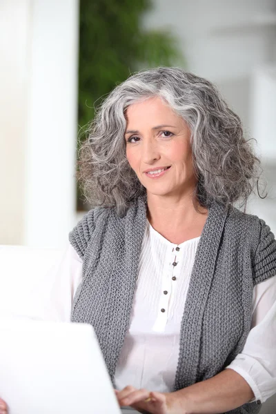 Grey-haired woman sat using laptop at home — Stock Photo, Image