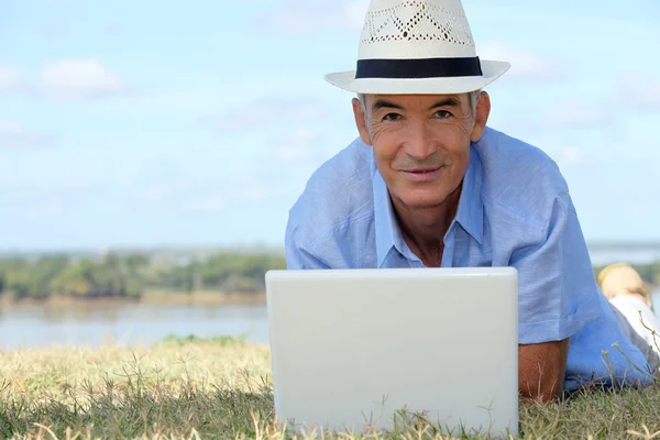 Homme âgé allongé sur l'herbe avec un ordinateur — Photo