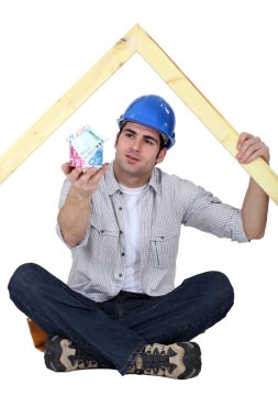 A carpenter presenting a miniature house made of euro bills. clipart