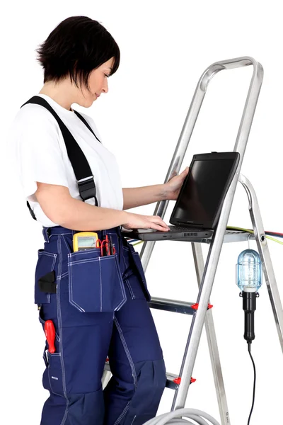 Female electrician resting laptop on rung of step-ladder — Stock Photo, Image