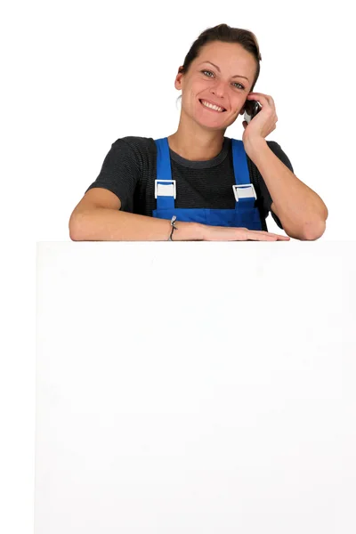 Kobieta w niebieski kombinezon z telefon i zarządu puste dla wiadomości — Zdjęcie stockowe