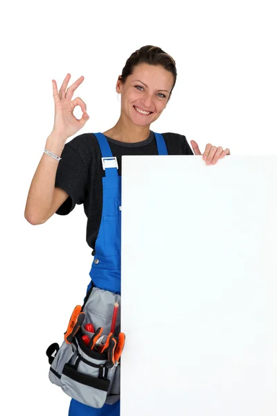 Female construction worker with tool belt and a board left blank for your message — Stock Photo, Image