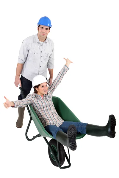 A construction worker carrying his female colleague in a wheelbarrow — Stock Photo, Image