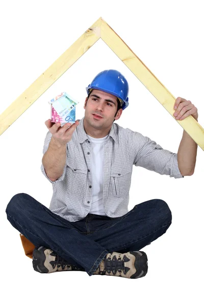 A carpenter presenting a miniature house made of euro bills. — Stock Photo, Image