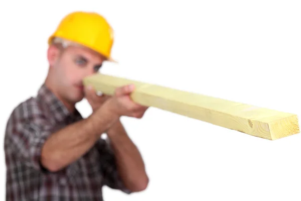 Carpinteiro olhando para baixo o comprimento de uma prancha de madeira — Fotografia de Stock