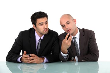 Perplexed man looking at his colleague's mobile phone clipart