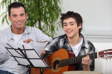 Adolescent boy learning to play the guitar clipart