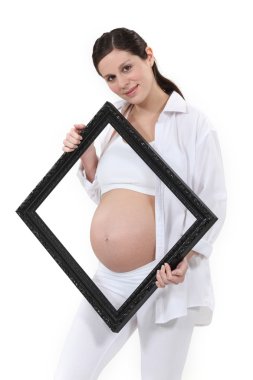 Pregnant woman holding a picture frame around her belly clipart