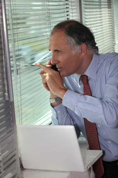 Un hombre de negocios mirando a través de las persianas . — Foto de Stock