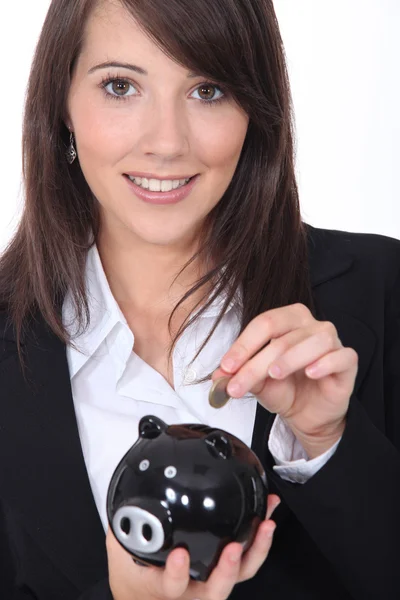 Jovem sorrindo colocando moeda em um banco porquinho — Fotografia de Stock