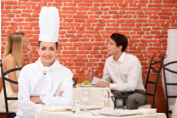 Vrouwelijke chef-kok poseren in restaurant met paar dineren in achtergrond — Stockfoto