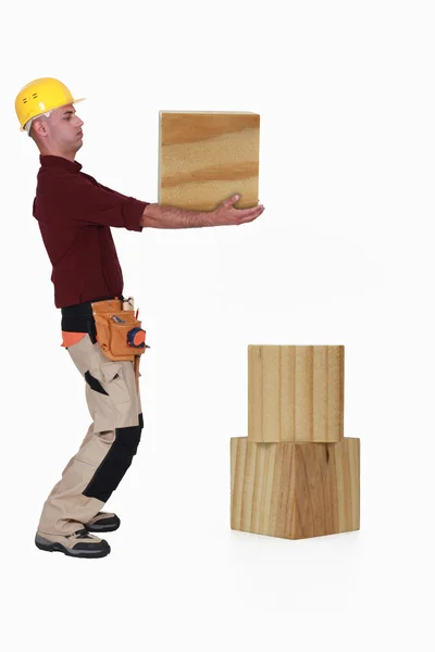Плотник поднимает тяжелый деревянный блок — стоковое фото