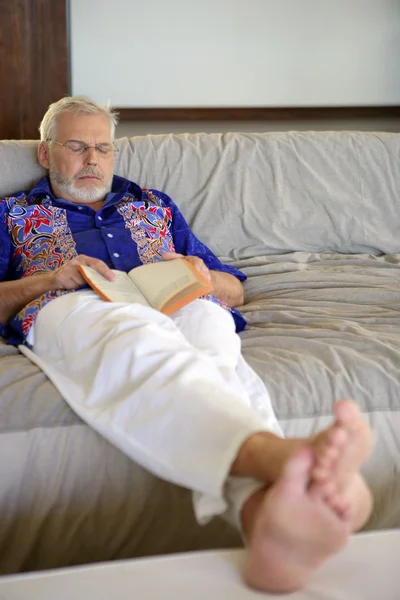 Sénior segurando um livro e dormindo no sofá — Fotografia de Stock