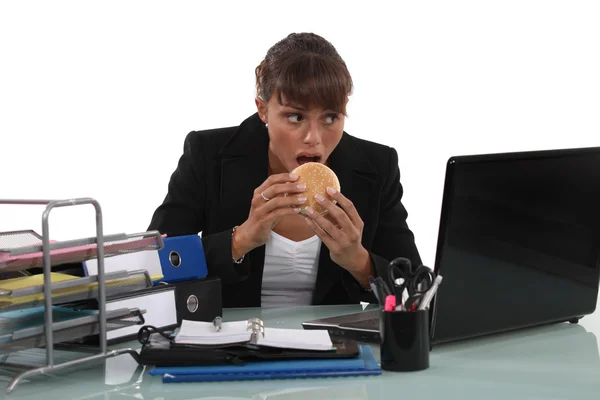 Kobieta jedząca burgera przy biurku — Zdjęcie stockowe