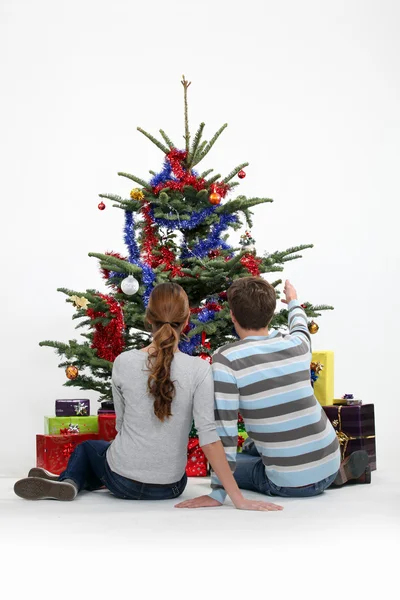 夫妇俩坐在圣诞树旁 图库照片