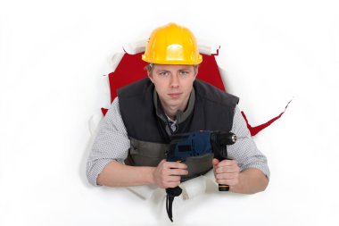 Craftsman posing in the hole of paper wall and holding a drill clipart