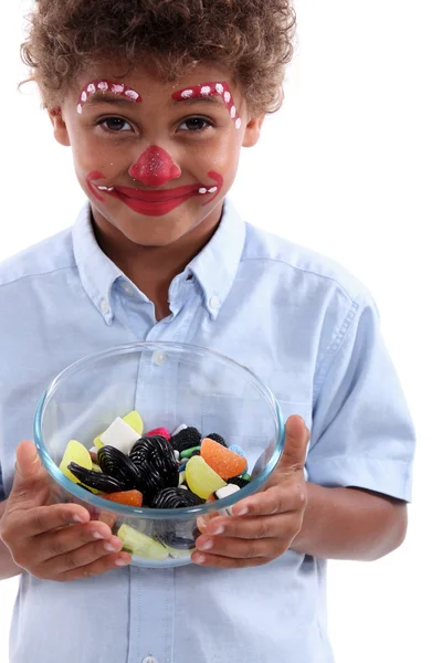 Kleine jongen geconfectioneerde als een clown met kom van snoep — Stockfoto