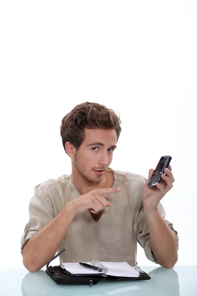Man with a ringbound agenda pointing at a cellphone — Stock Photo, Image