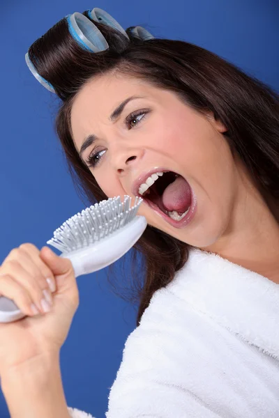 Kobieta z lokówki i szczoteczkę do zębów w ręku śpiew — Zdjęcie stockowe